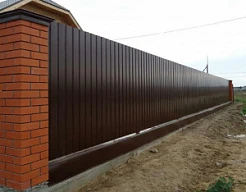 Забор из профлиста коричневого цвета на кирпичных столбах
